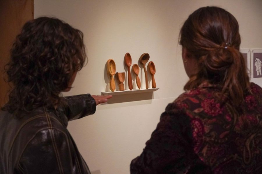 Two gallery attendees stand looking at Kelly Banfield's piece "Sisterhood of the Traveling Spoons."