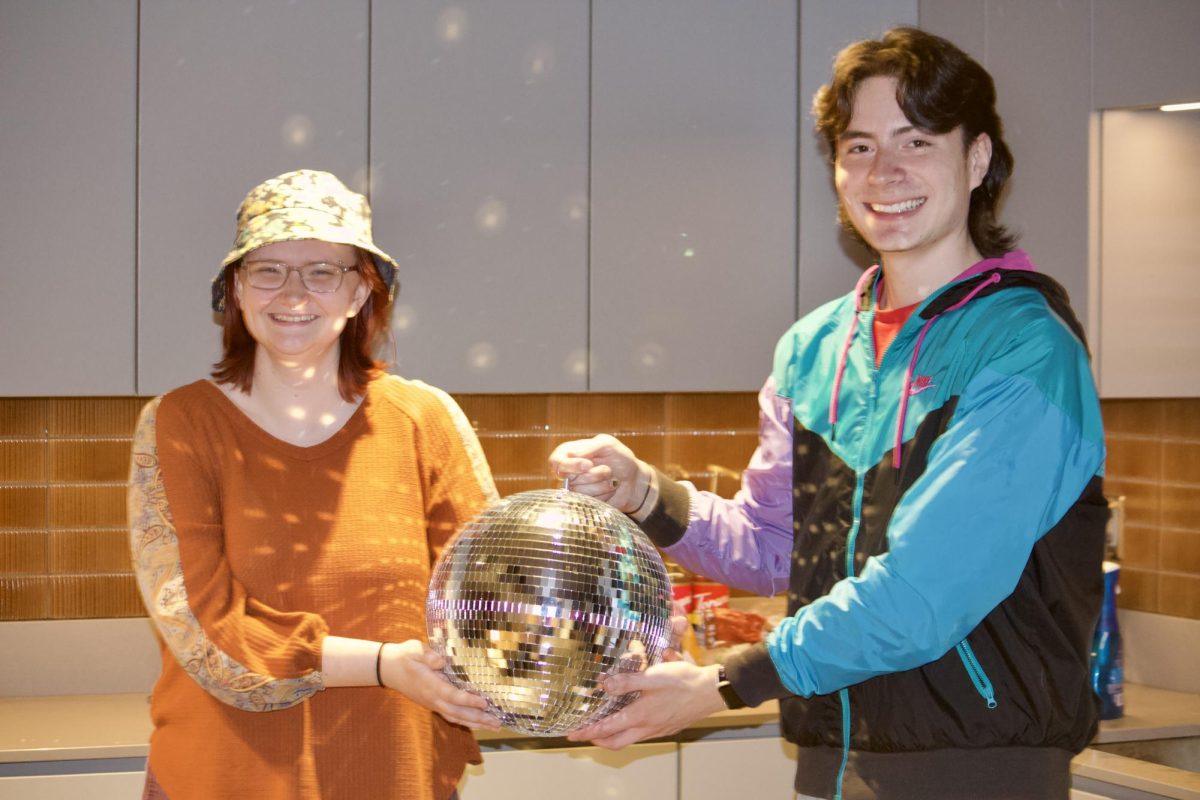 From left: Jules Wood `25 and Adam Figueras `25 hold a disco ball in their Renfrow apartment. 